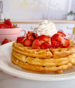 Stacked waffles on a white plate with fresh berries.