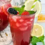 Tall glass of triple lemonade with mint and berries.