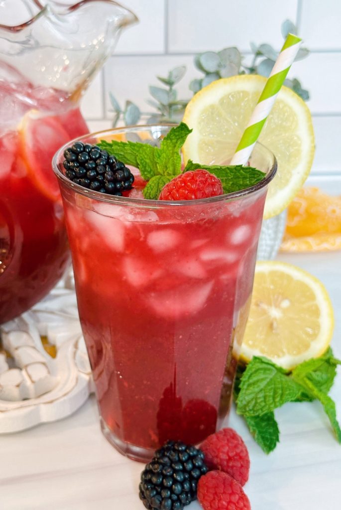 Tall glass of triple lemonade with mint and berries.