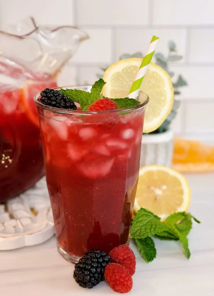 Tall glass of Triple Berry Lemonade with a green and white striped straw.