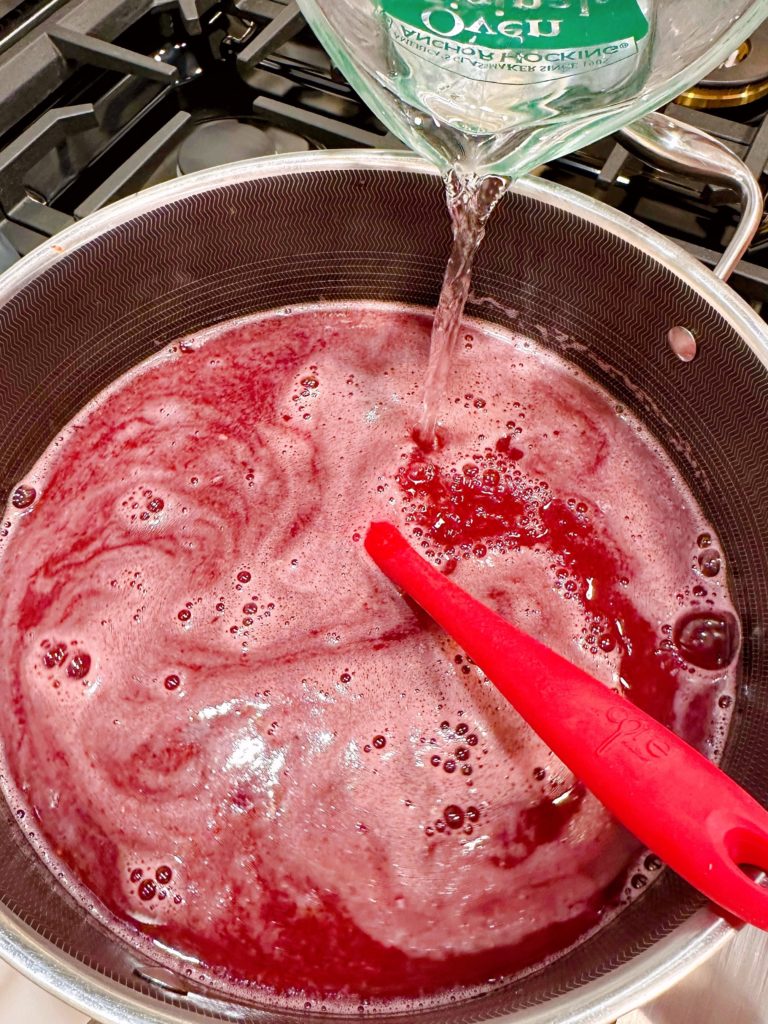 Adding the remaining water to the berry lemonade mixture in the pot.