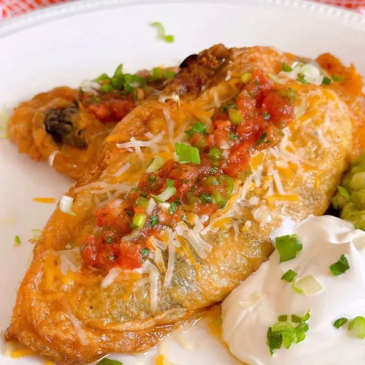 Chile Rellenos on a plate with salsa, quacamole, and sour cream.