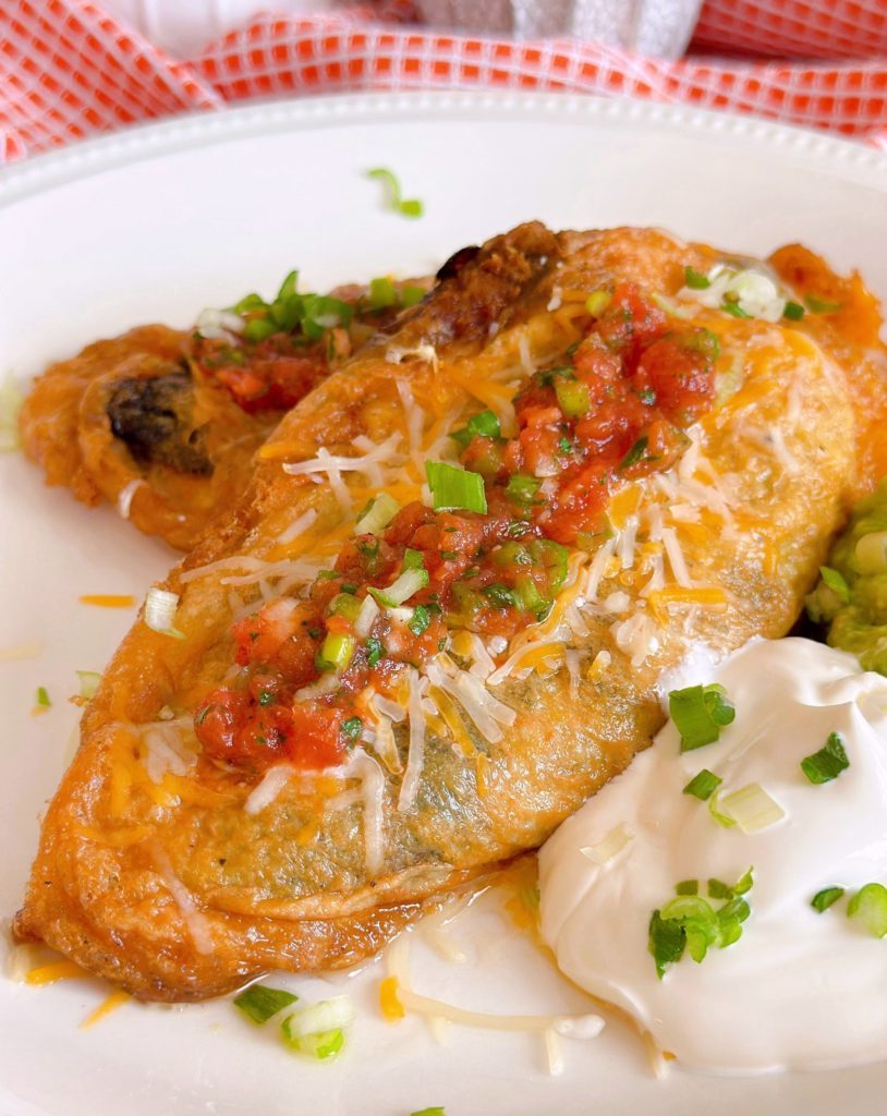 Chile Rellenos on a plate with salsa, quacamole, and sour cream.