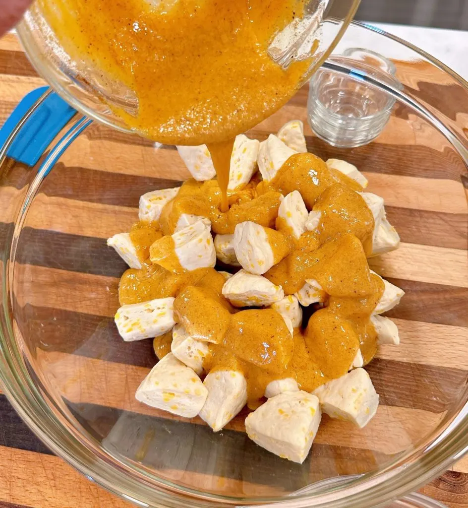 Pouring pumpkin mixture over cut biscuits.