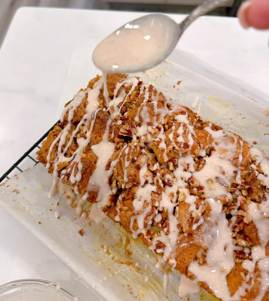 Baked Pumpkin Spice Bubble Bread on a cooling rack with spiced glaze being drizzled over the top.