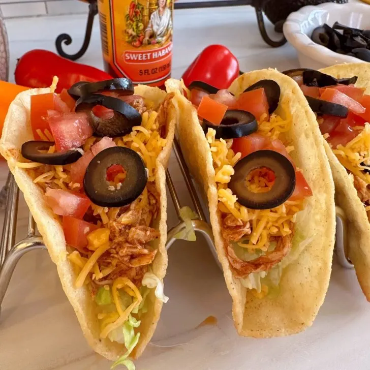 Chicken tacos in a stand with toppings.