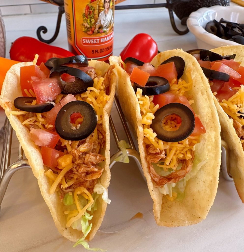 Chicken tacos in a stand with toppings.