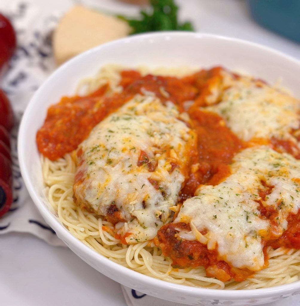 Chicken Parmesan cutlets in a bowl with sauce and pasta.