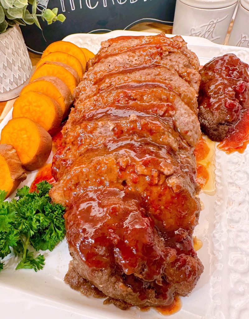 Brown Sugar Meatloaf sliced and on a platter with glaze drizzled over the top with sweet potato medalions.