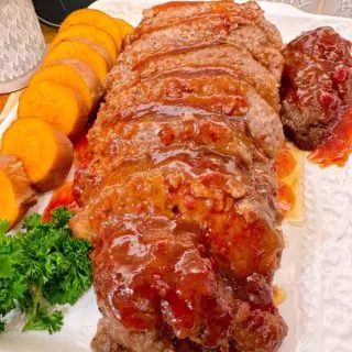 Brown Sugar Meatloaf sliced and on a platter with glaze drizzled over the top with sweet potato medalions.