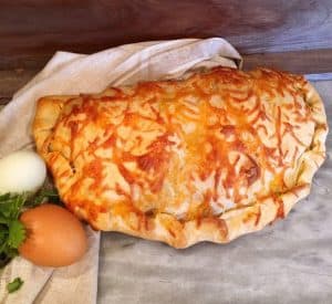 Whole breakfast calzone on a board with eggs.