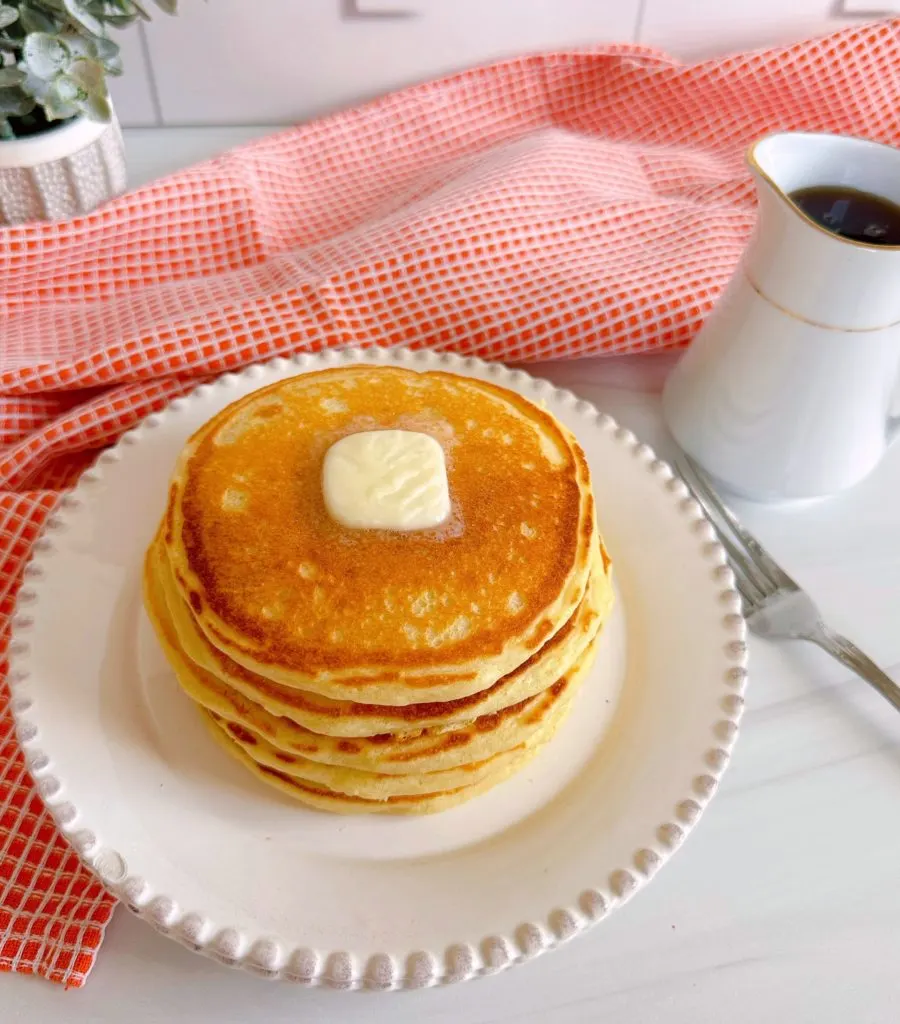 Stack of pancakes on a plate with a pat of butter.