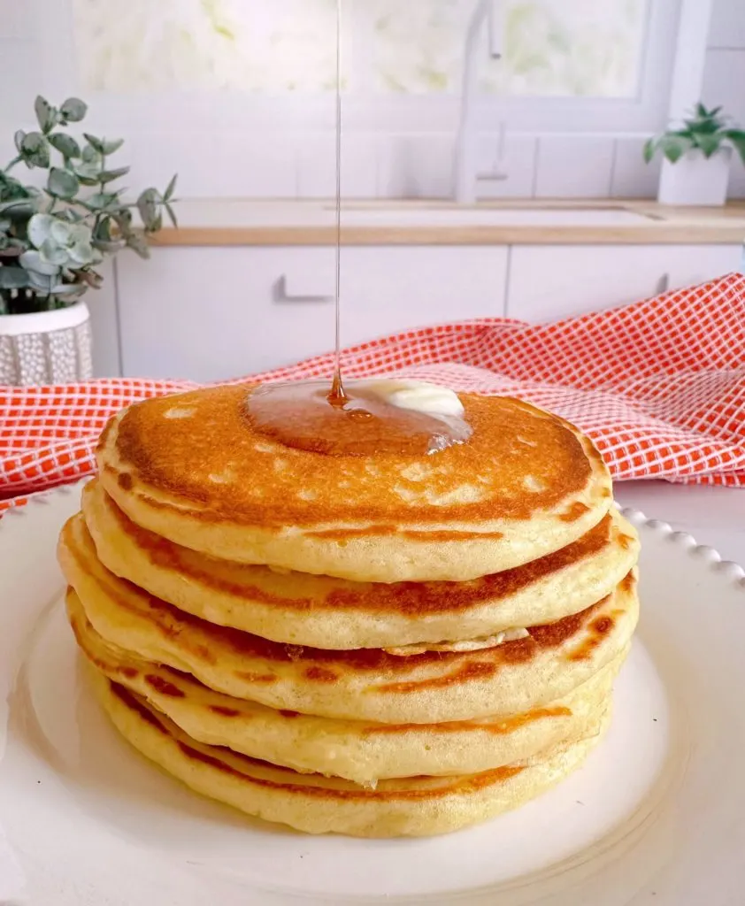 Syrup pouring over a stack of buttermilk pancakes.