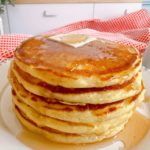 Tall stack of pancakes with syrup and butter.