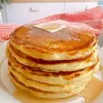 Tall stack of pancakes with syrup and butter.