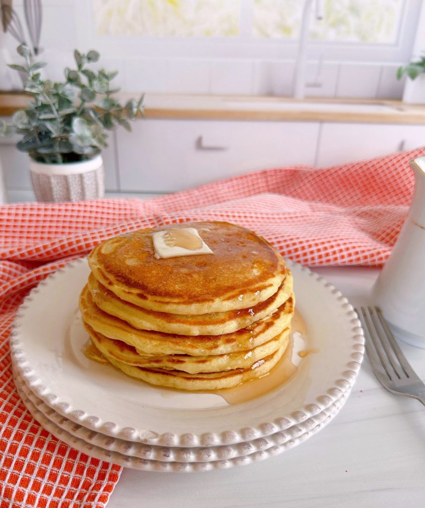 Stack of buttermilk pancakes with syrup and butter on a white plate.