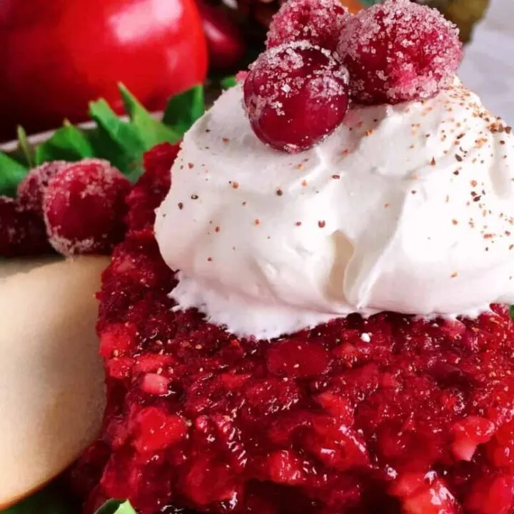 Cranberry Apple Jello Salad with whippped cream and frosted cranberries on a plate with lettuce.