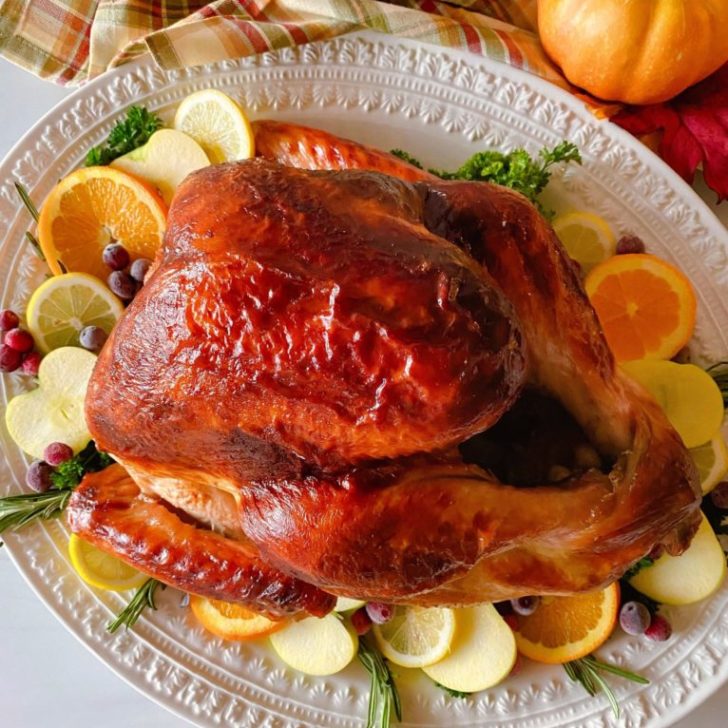 Roasted Turkey on a white platter with fruit slices surrounding it.