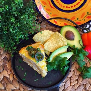 Slice of layered slow cooker chicken enchilada casserole on a cast iron skillet. Topped with jalapenos, served with corn chips and sliced avocados.