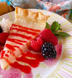 A beautiful slice of Depression Era Water Pie with raspberry sauce and fresh berries on a pretty plate.