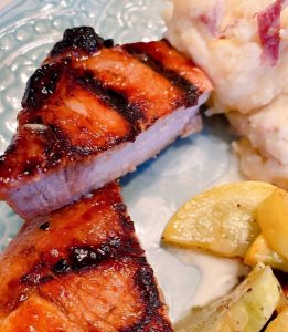 Grilled Pork Chop cut in half on a dinner plate with squash and potatoes.