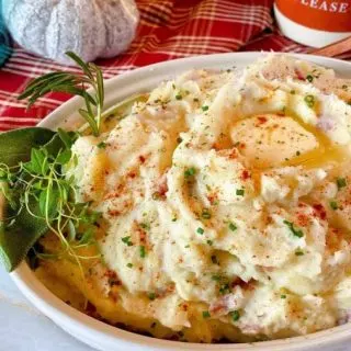 Close up photo of bowl filled with creamy instant pot mashed potatoes with fresh herbs.