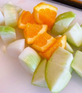 Orange, apple, and onion chunks on cutting board for stuffing hens