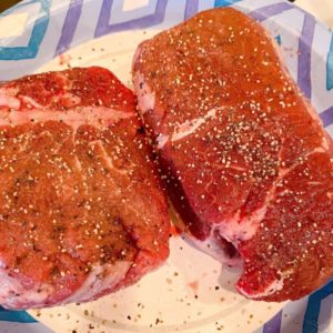 Filet Mignon on a paper plate resting before cooking, and seasoned with salt and pepper.