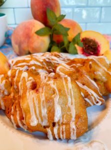 Fried Peach Fritters on a plate with fresh peaches in the background.