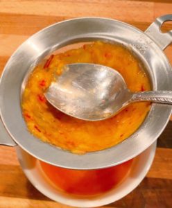 Mashed peaches poured into a strainer, pressing the peaches into the strainer to remove all juice.