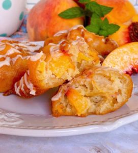 Fresh Peach Fritter opened up to see inside on a white plate with fresh peaches in the background.