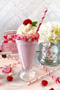 White Chocolate Raspberry Milkshake in an old fashioned glass topped with whipped cream and a fresh raspberry.