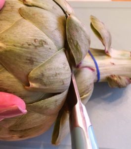 Trimming the stem off the artichoke on a cutting board.