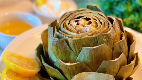 Steamed Artichoke with lemon slices in a serving bowl.