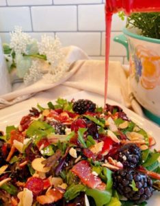 Pouring dressing over serving of Blackberry Spring Salad.