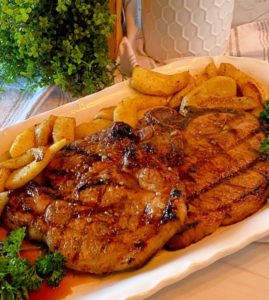 Grilled Honey Garlic Bone-in Pork Chops with fried apple slices on a white serving platter.