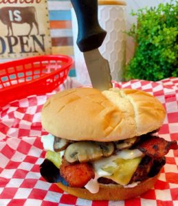 Blue Cheese Bacon Mushroom Burger on a red checkered paper with a knife stabbed through it to hold it together.