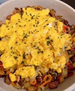 Adding scrambled eggs to cooked skillet veggies and meats. Topped with more chopped chives.