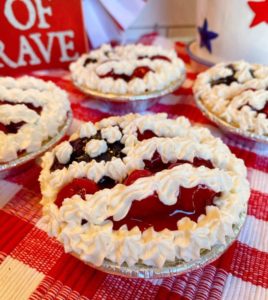 Mini No Bake Patriotic Cheesecake Pies with cherry and blueberry pie filling decorated like a flag on a red and white plaid cloth.