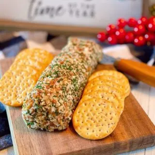 Salmon Party Log on a small cutting board with crackers and holiday decor in the background.