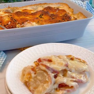 Creamy Cheesy Au Gratin Red Potatoes in a casserole dish with a serving on white plates stacked.