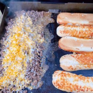 Cheese on ground beef with buns toasting on Black Stone.