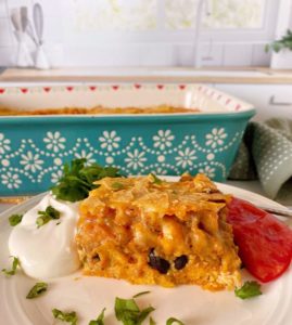 Breakfast Ranchero Egg Bake Casserole with a large serving on a plate surrounded by sour cream and freshly sliced tomatoes.