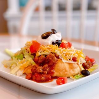 Navajo Taco on a white square plate loaded with all the toppings on a table.