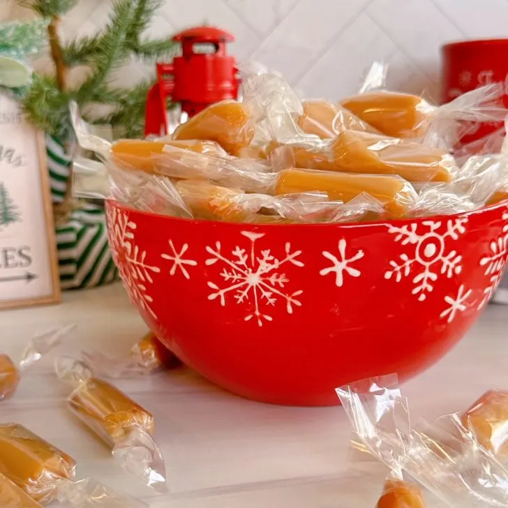 Homemade Caramels in a bright red candy dish on the kitchen counter.