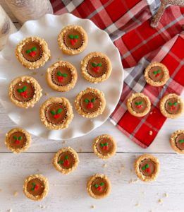 Overhead shot of Christmas Peanut Butter Cup cookies on a white cake plate and a plaid dish cloth.