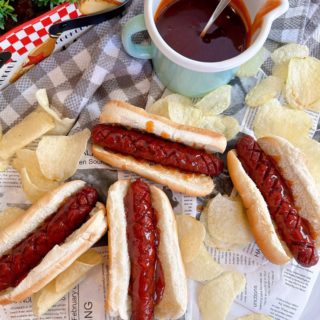 J. Dawgs on a table in buns with special sauce and a measuring cup with extra sauce.