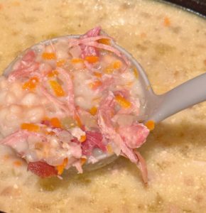 Navy bean soup in a ladle over the slow cooker after cooking 4 hours.