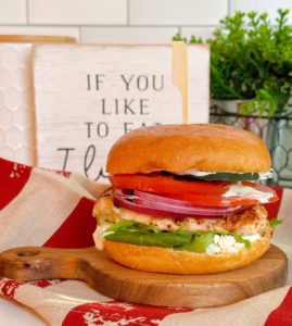 Gilled Mediterranean Chicken Sandwich on a small cutting board with all it's layers of deliciousness.