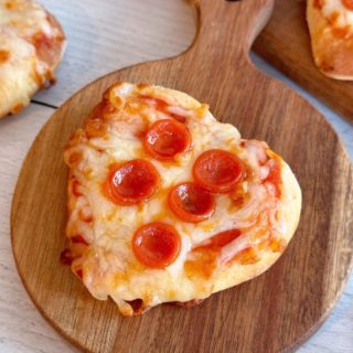 Close-up photo of a mini air fryer pepperoni pizza on a small cutting board.